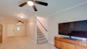 A living room with a large flat-screen TV, a wooden cabinet, a ceiling fan, and a staircase. - Dock Access: Waterfront Studio in Colonial Beach! (Colonial Beach)
