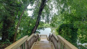 A wooden bridge leading to a body of water surrounded by dense greenery. - Dock Access: Waterfront Studio in Colonial Beach! (Colonial Beach)