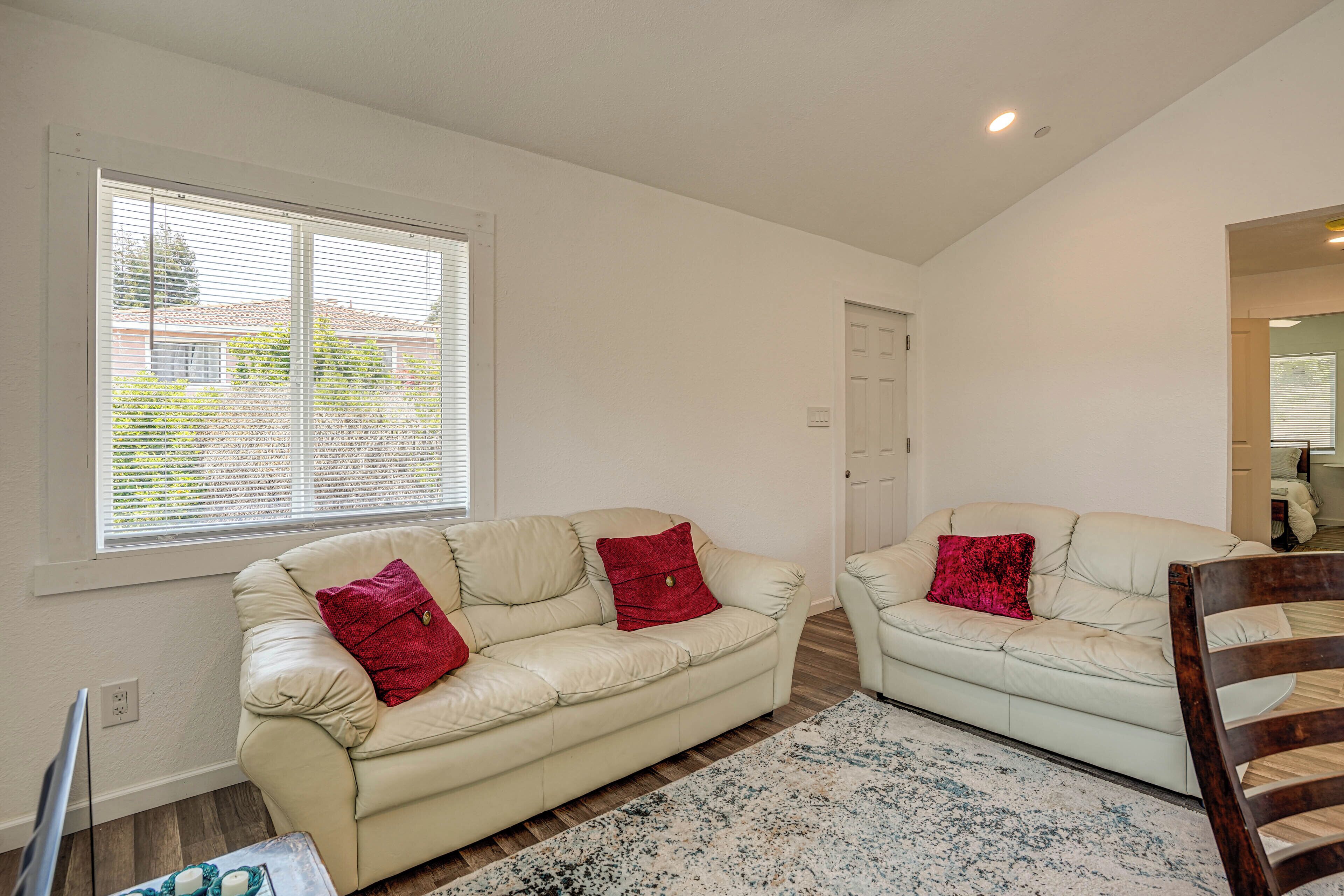 A living room with two cream-colored sofas, each with a red pillow, a patterned rug, and a wooden chair.