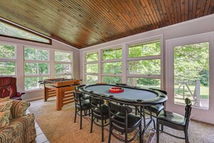 Una habitación con mesa de billar, cuatro sillas, mesa de fútbol de mesa y grandes ventanales con vistas a árboles.
