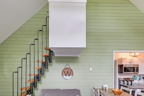 A staircase with black and wooden steps, a white wall with a 'W' sign, a gray couch, and a kitchen area with a microwave and stove. - Pool & Marina Access: Lewes Home w/ Fenced Yard! (Lewes)