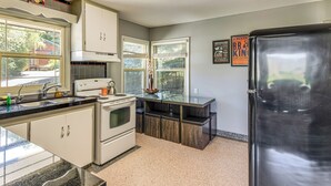 Una cocina con armarios blancos, un refrigerador de acero inoxidable y una ventana con persianas.