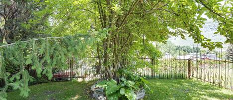 A fenced garden with a tree, grass, and a metal fence.