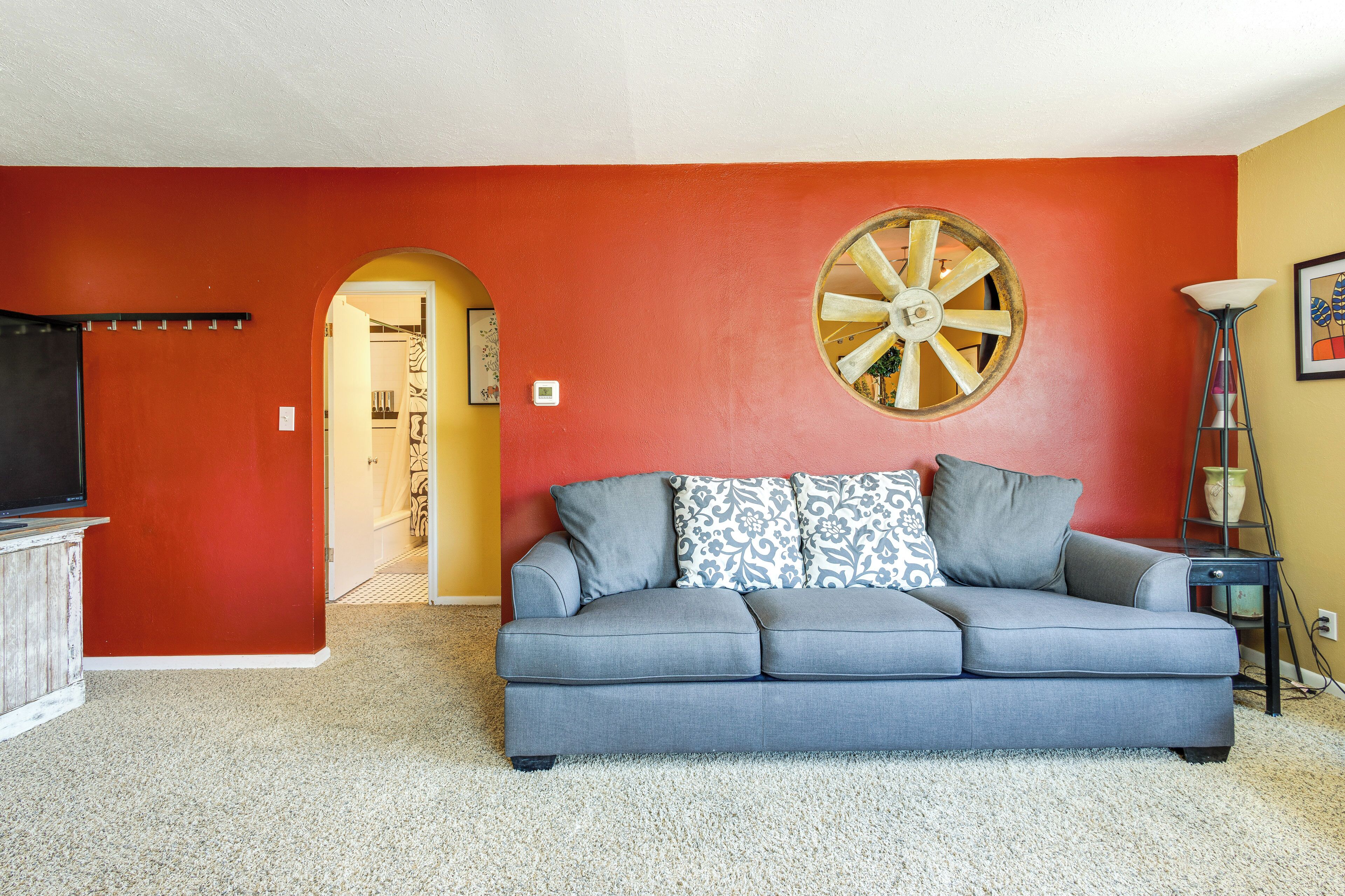 A living room with a grey sofa, a large decorative wheel, and a television on a wooden cabinet.