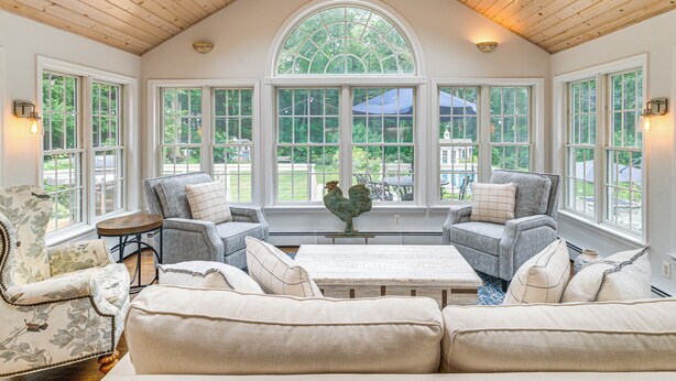 A spacious room with a high ceiling, large windows, and a central seating area with sofas and a coffee table. - Pool, Gardens & Hot Tub: Luxe Sandy Hook Home! (Sandy Hook)