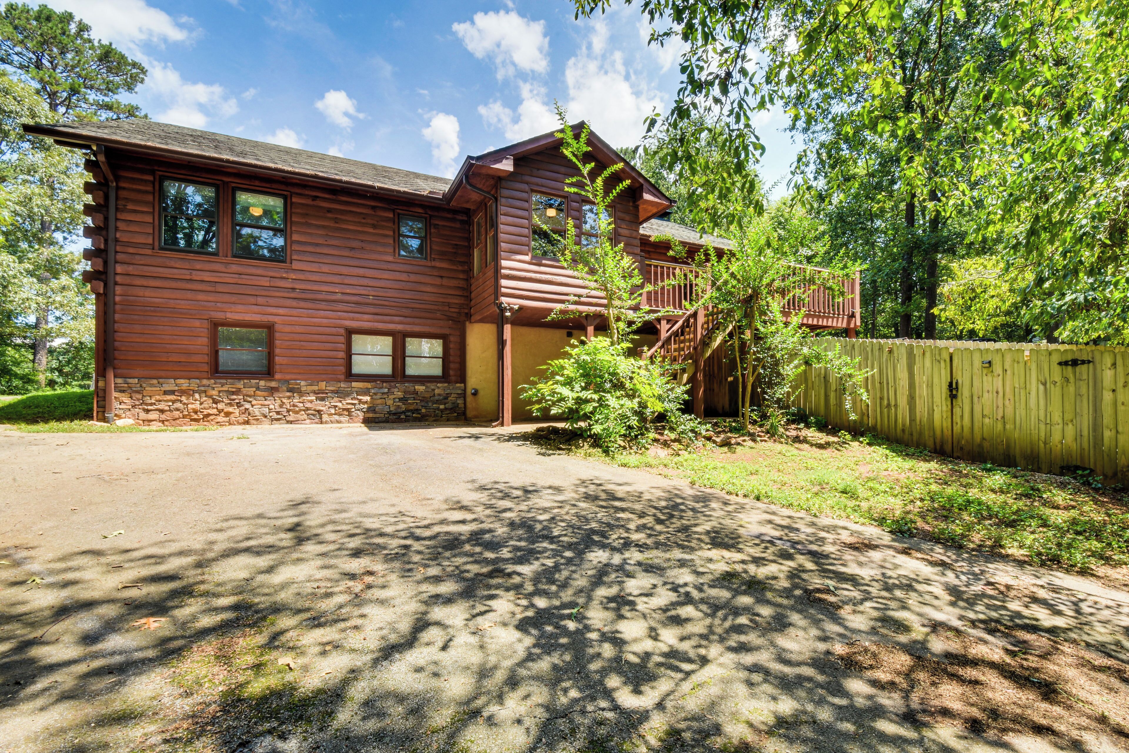 A two-story wooden house with a stone foundation, a front porch, and a wooden fence.