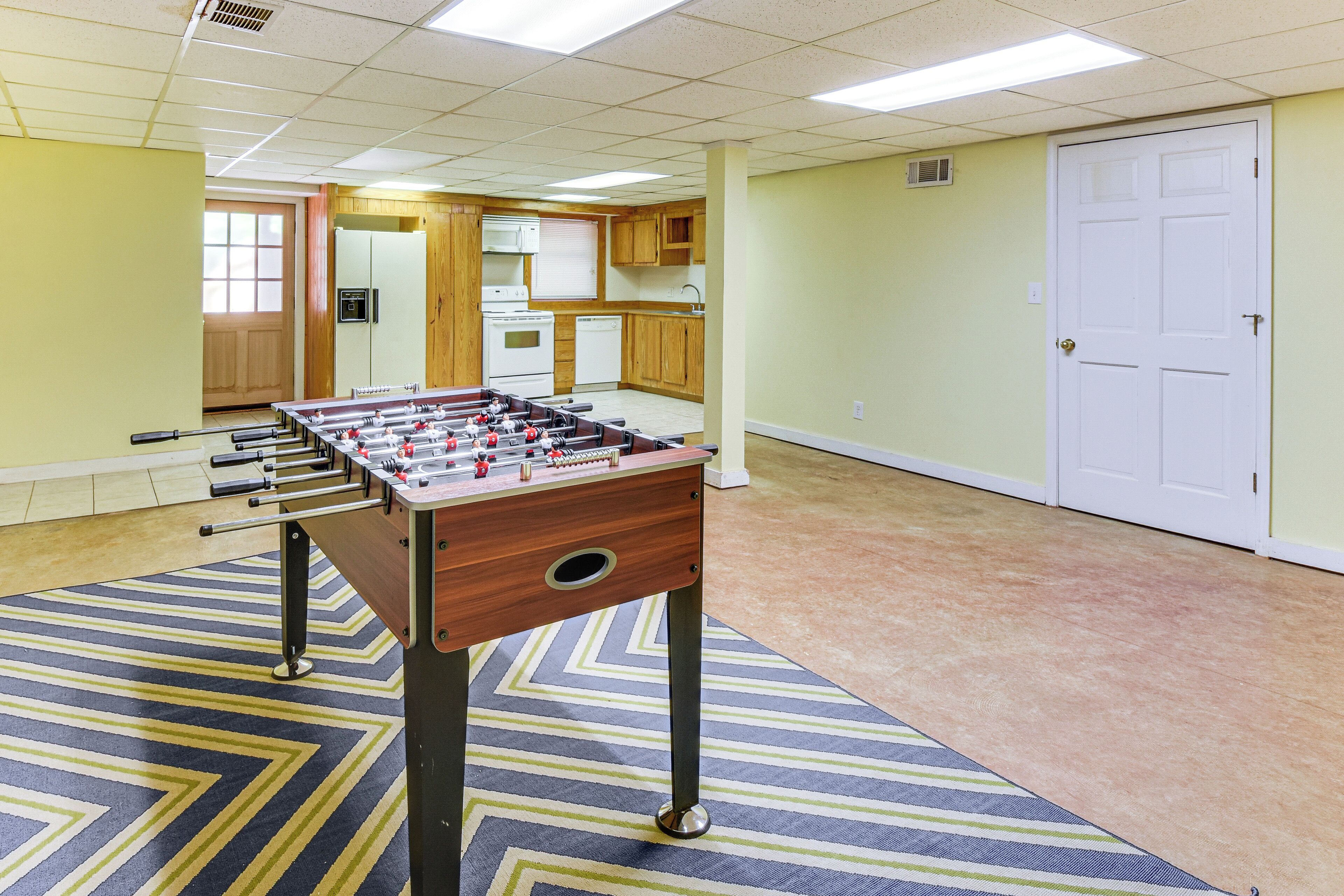 A room with a foosball table, wooden cabinets, a kitchenette, and a door.