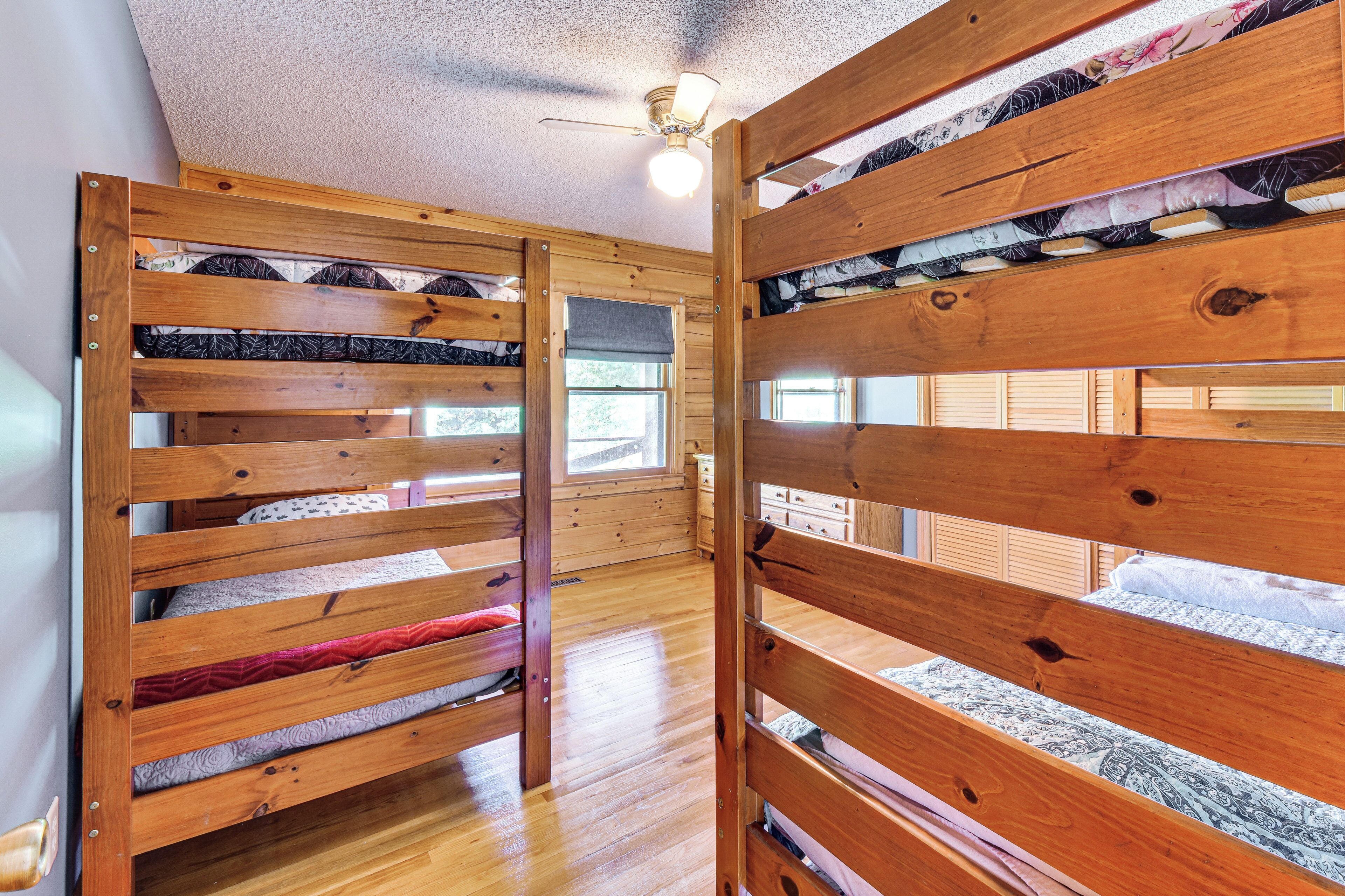 A room with bunk beds, wooden walls, a ceiling fan, and a window.