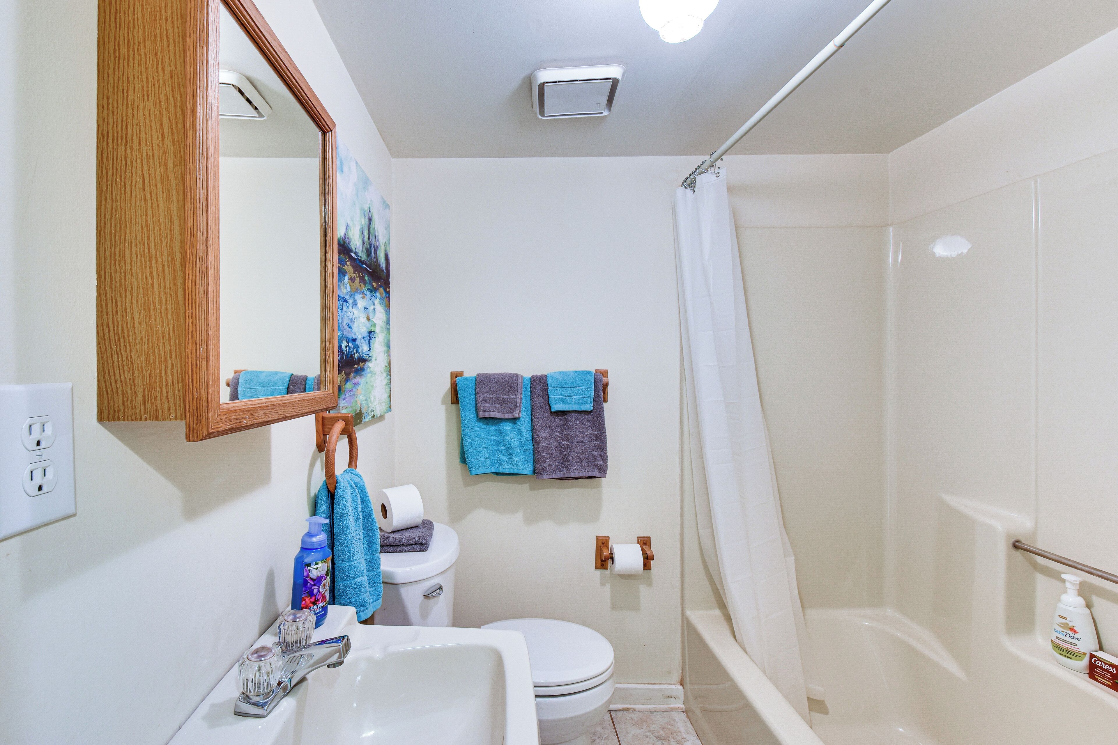 A bathroom with a white sink, toilet, and bathtub. There are towels hanging on the wall, a mirror, and a shower curtain.