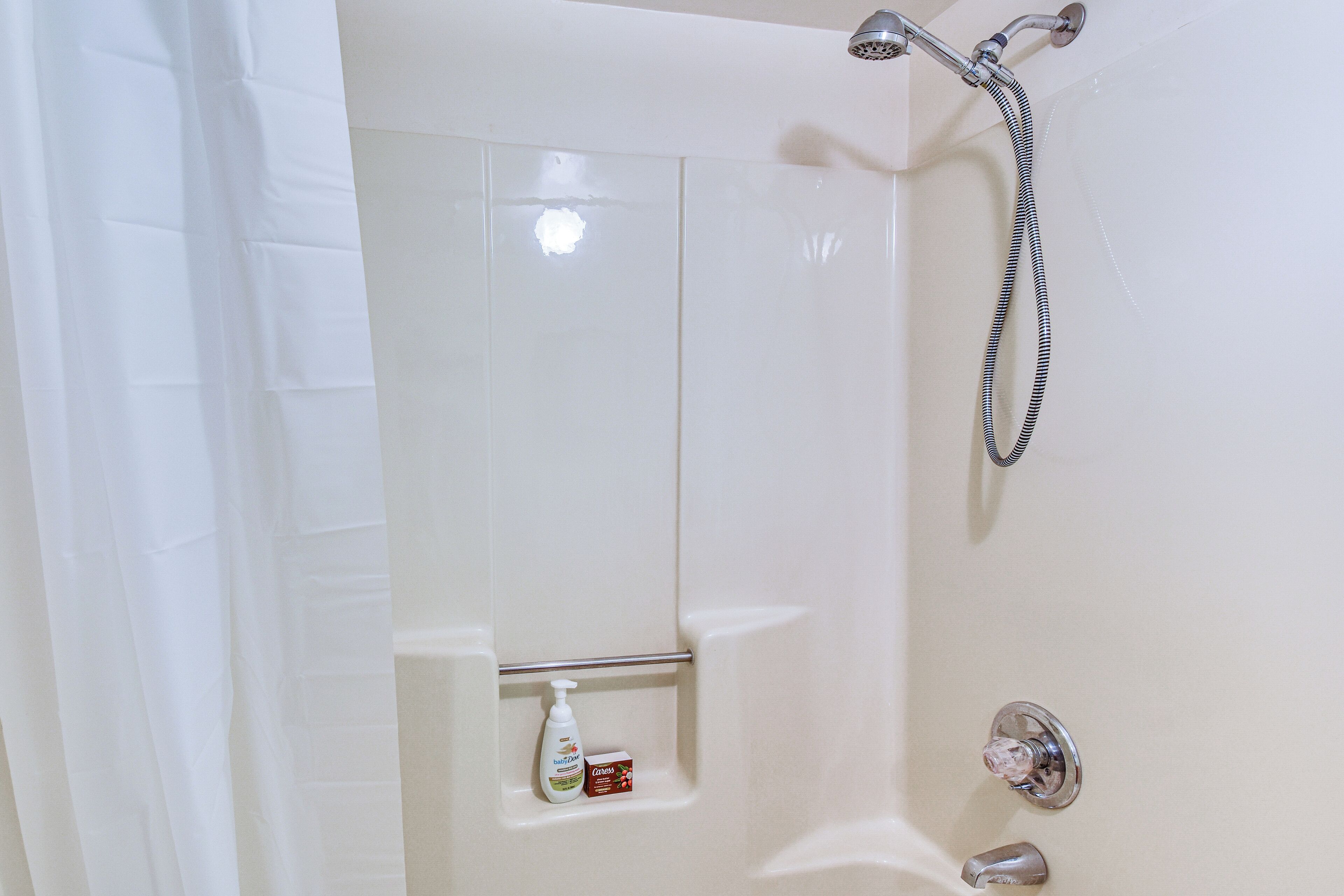 A bathroom with a shower, a hand soap dispenser, and a toothbrush holder.