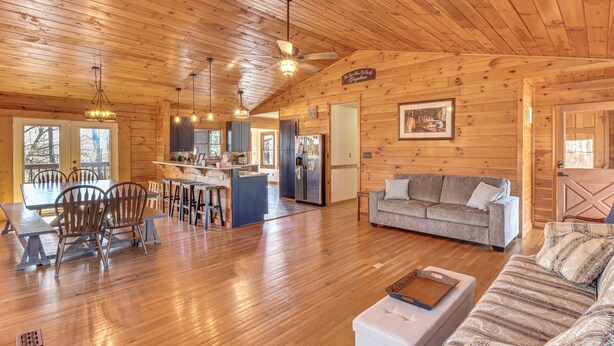 A spacious cabin interior with a wooden ceiling, a dining area with a table and chairs, a sofa, and a kitchen area with a refrigerator and cabinets. - Woodsy Hideaway: 8 Mi to Henderson Falls Park! (Toccoa)