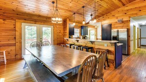 A wooden cabin interior with a large dining table, wooden chairs, a kitchen area, and a refrigerator. - Woodsy Hideaway: 8 Mi to Henderson Falls Park! (Toccoa)
