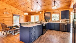 A spacious kitchen with wooden walls, a large island, dark cabinets, and modern appliances. - Woodsy Hideaway: 8 Mi to Henderson Falls Park! (Toccoa)