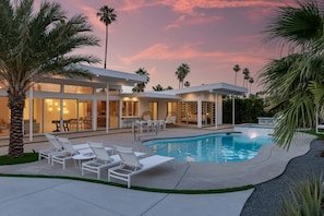 A modern house with a swimming pool, outdoor seating, and palm trees.