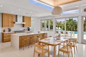 A modern kitchen with a central island, wooden cabinets, and a large window overlooking a pool area.
