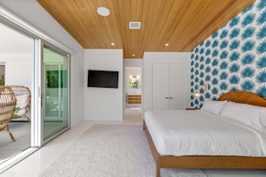 Quarto com cama, televisão, porta de correr de vidro para uma varanda e parede estampada.
