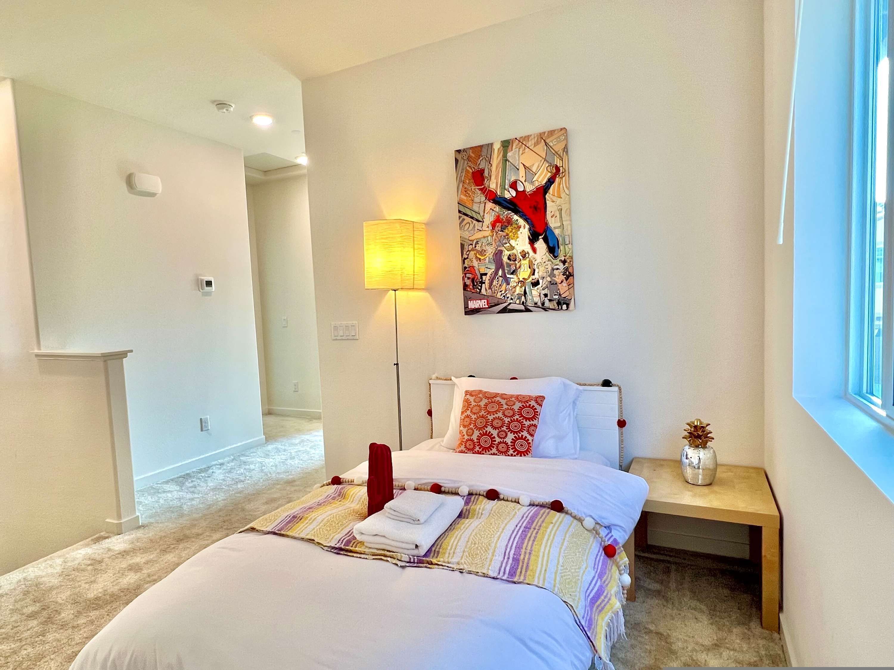 A bedroom with a bed, a wall-mounted lamp, a painting, and a window.