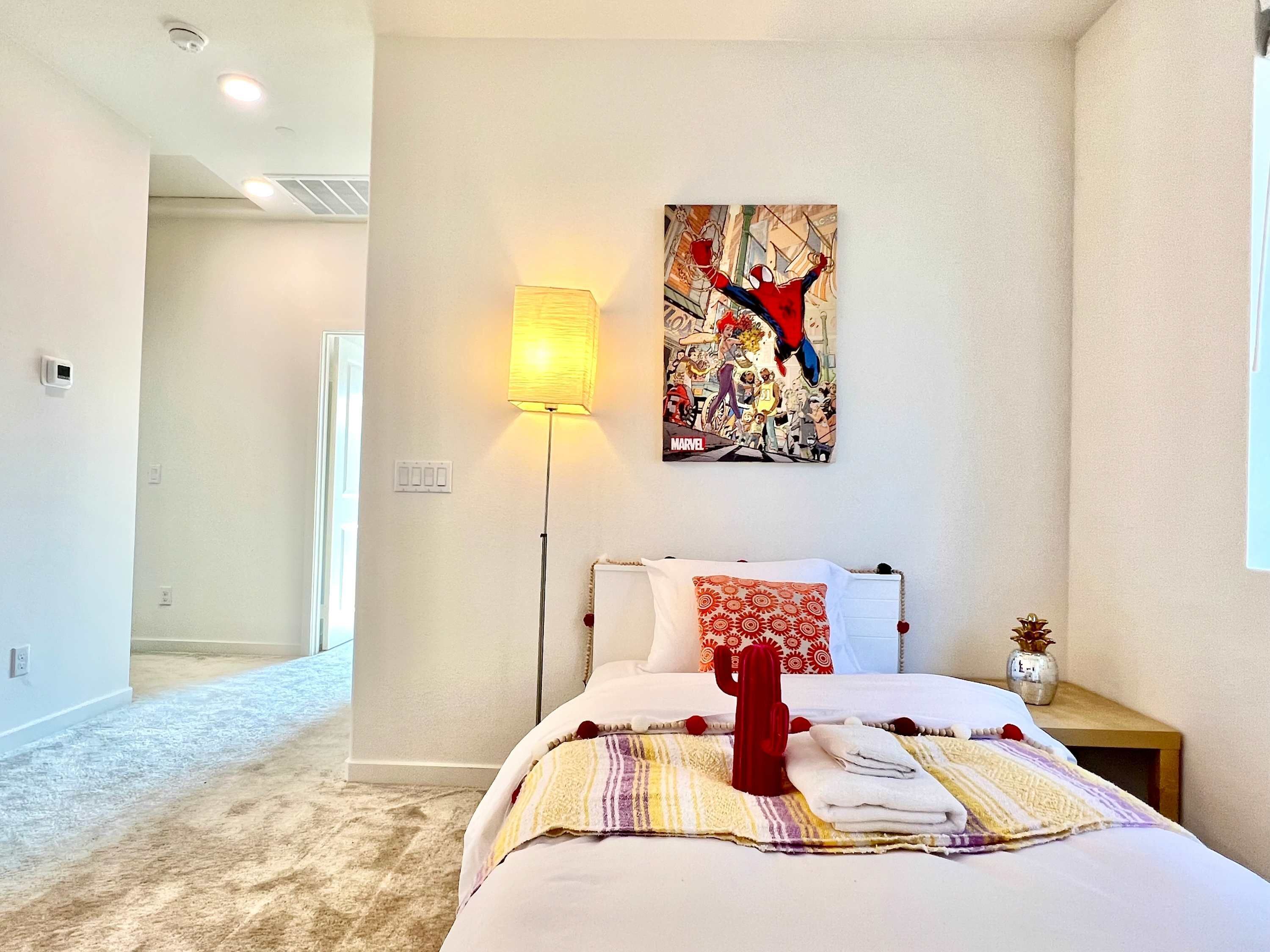 Una camera d'albergo con un letto, una lampada, un quadro e un comodino con un vaso.