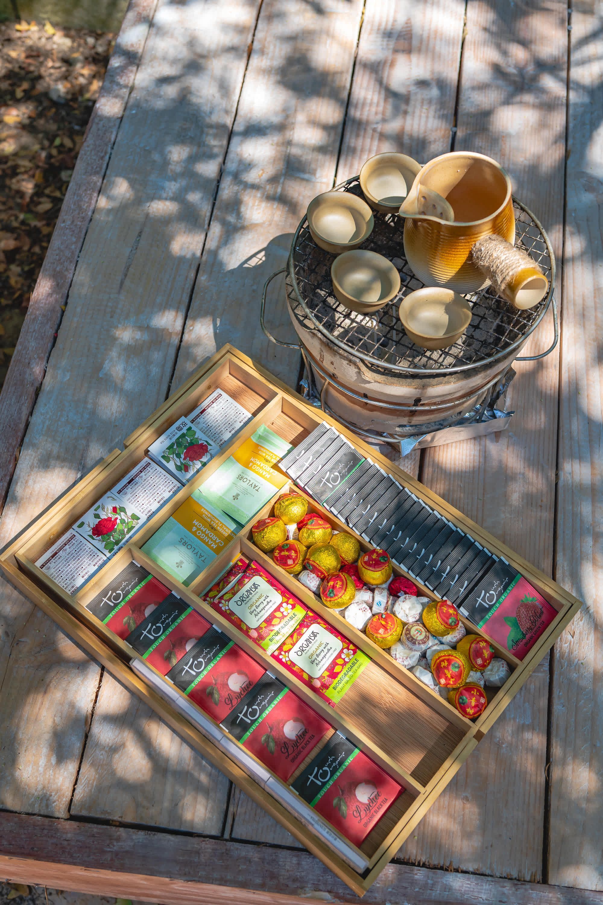 Un tavolo da picnic in legno con un cesto di bustine di tè e una griglia con tazzine.