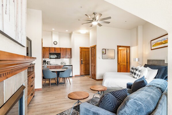 A modern hotel room with a bed, a sofa, a dining area, and a kitchen.