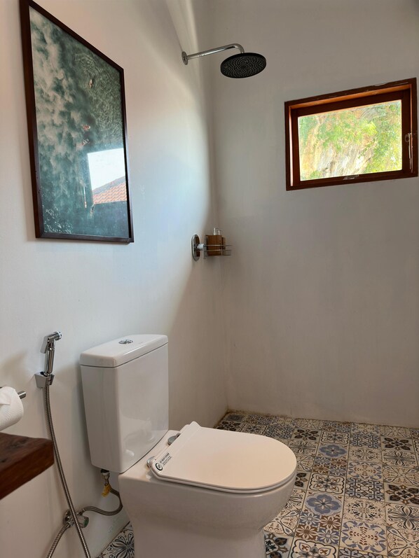 Une salle de bain avec des toilettes, une douche et une petite fenêtre.