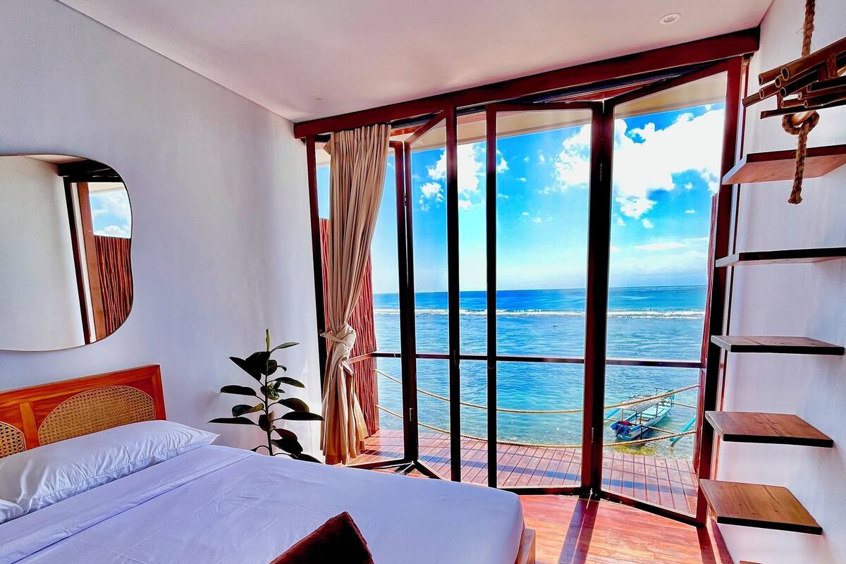 A bedroom with a large bed, a view of the ocean, and a wooden floor.
