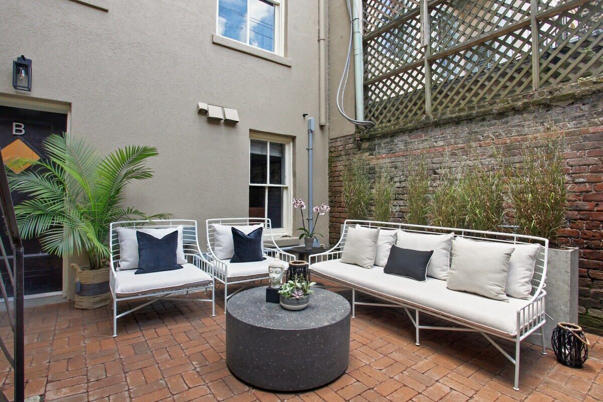 Un patio con un conjunto de sofá y mesa redonda de metal blanco, y macetas con plantas.