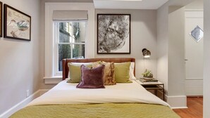 A bedroom with a bed, pillows, a nightstand, a framed picture, and a window. - Cozy 1BR Historic Condo | Downtown Savannah (Savannah)