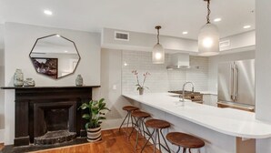 A modern kitchen with a white countertop, bar stools, a fireplace, and stainless steel appliances. - Cozy 1BR Historic Condo | Downtown Savannah (Savannah)