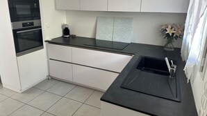 Una cocina moderna con armarios blancos, horno empotrado, cafetera y un florero con flores en la encimera.