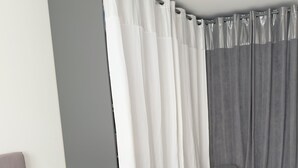 Un dormitorio con una cama, un taburete pequeño y una cortina gris.