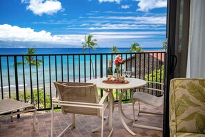 Een balkon met een tafel voor twee, met uitzicht op een strand met palmbomen en de oceaan.