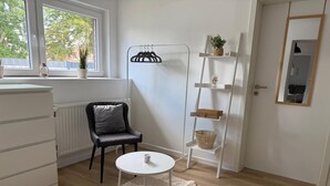 A room with a white radiator, a grey chair, a white table with a basket, a floor lamp, and a mirror on the wall. - Cozy vacation apartment in the heath (Hodenhagen)