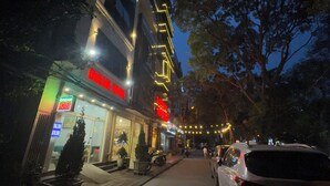 A hotel with a neon sign, outdoor seating, and a street view. - Dream Hotel (Hanoi)