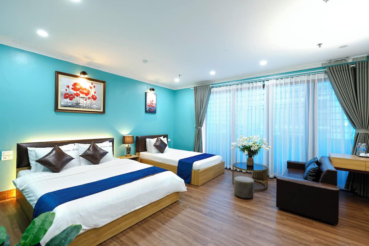 Habitación de hotel con dos camas, un escritorio, un sofá y un ventanal con cortinas.