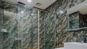 A modern bathroom with a glass-enclosed shower, a marble wall, and a white sink. - Dream Hotel (Hanoi)