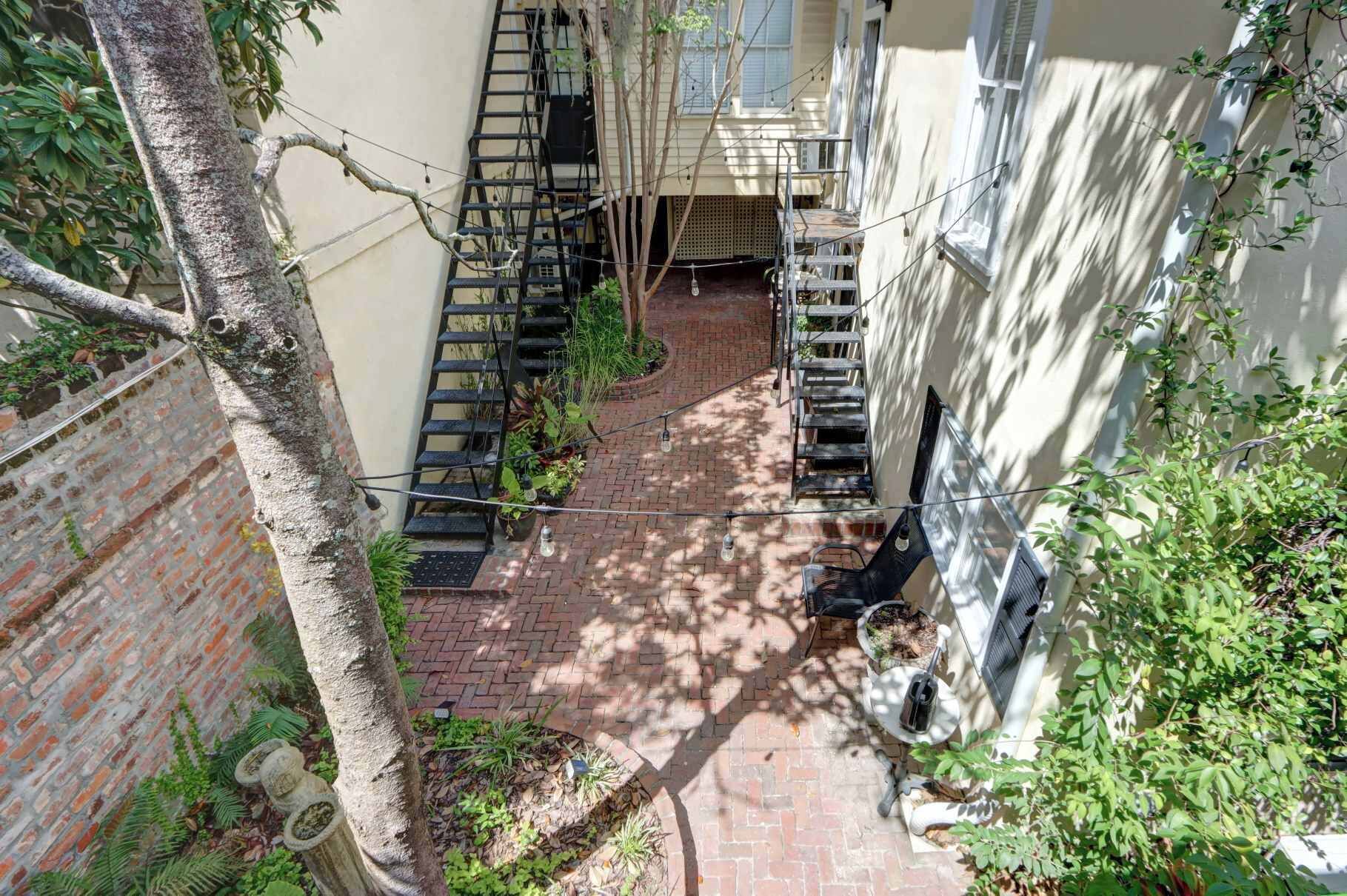 A narrow brick pathway flanked by buildings, with a metal staircase on one side and a white wall on the other.