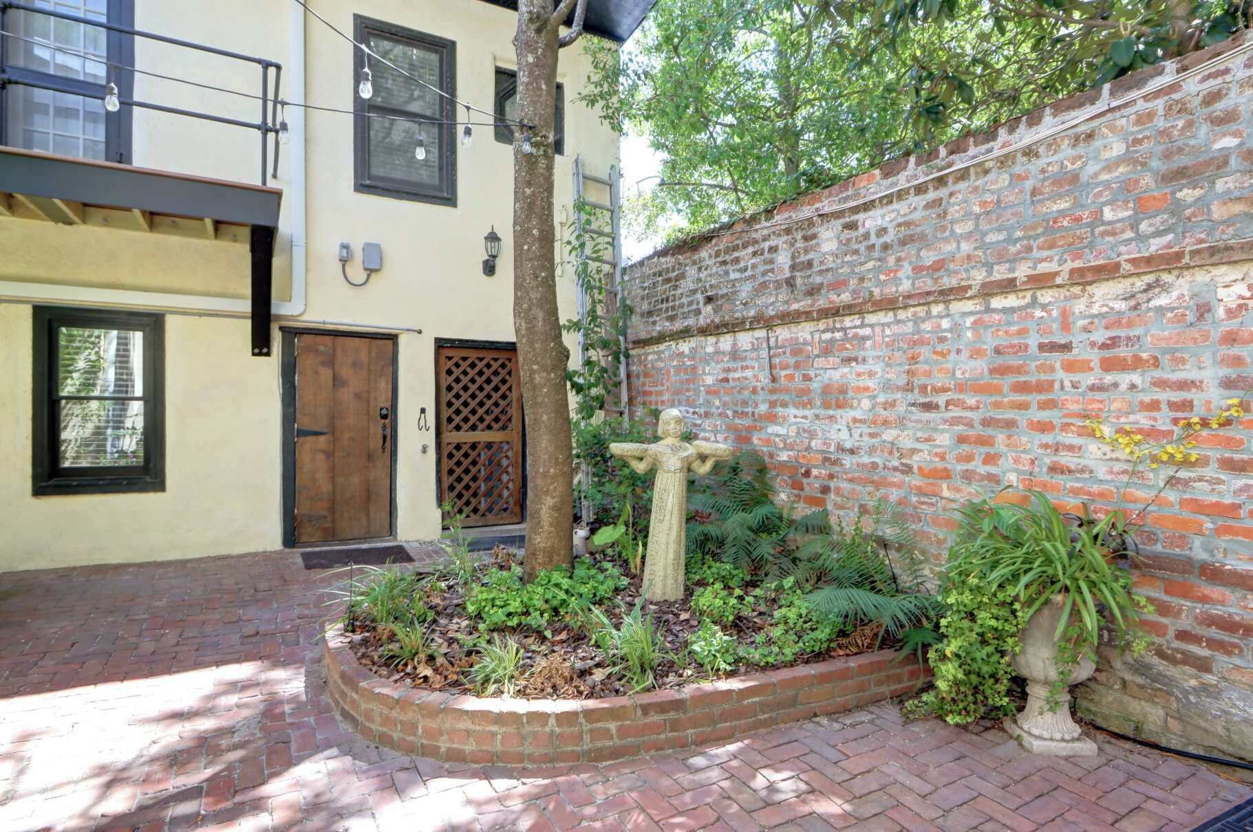 Un patio con muro de ladrillo, puerta de madera y estatua de piedra.