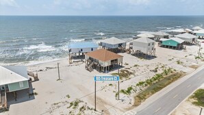 Une zone côtière avec des maisons sur pilotis, une route et un panneau indiquant « 105, allée du Trésor ».