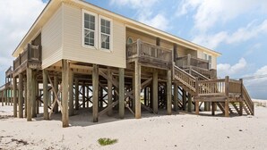 Une maison située en bord de mer, dotée d’une terrasse en bois et d’un escalier menant à l’entrée principale.