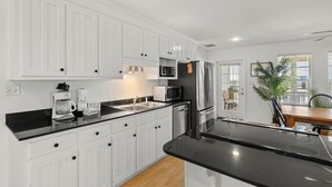 Une cuisine moderne avec des meubles blancs, des plans de travail noirs, des appareils en acier inoxydable et un coin repas comprenant une table et des chaises en bois.