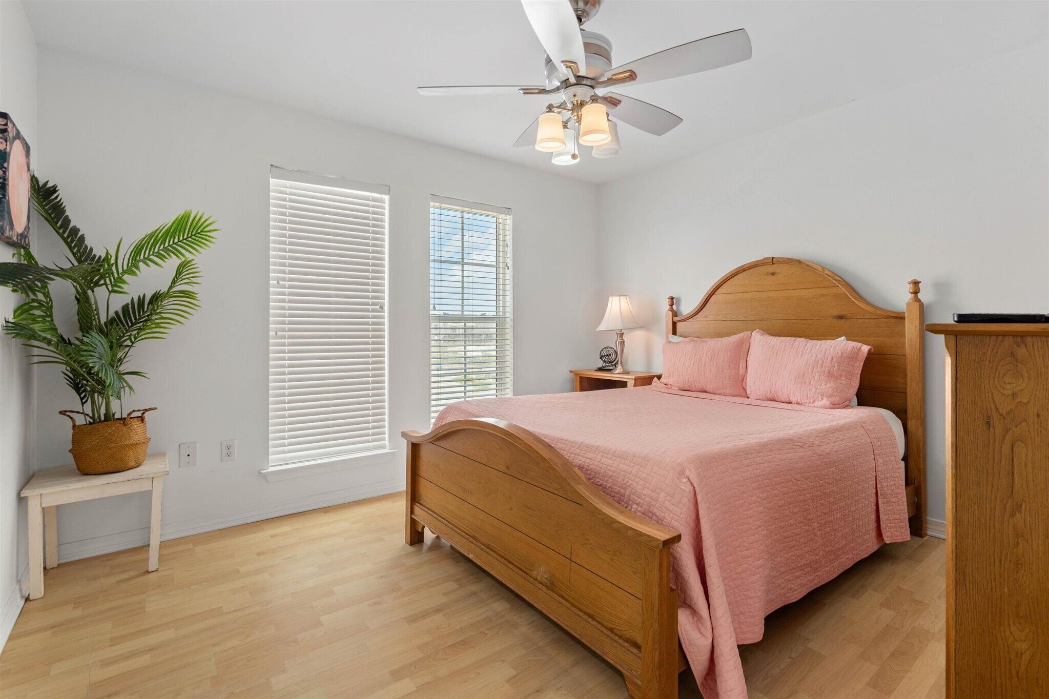 Makuuhuoneessa on puinen sänky, kattotuuletin, yöpöytä lampun kanssa ja ruukkukasvi.