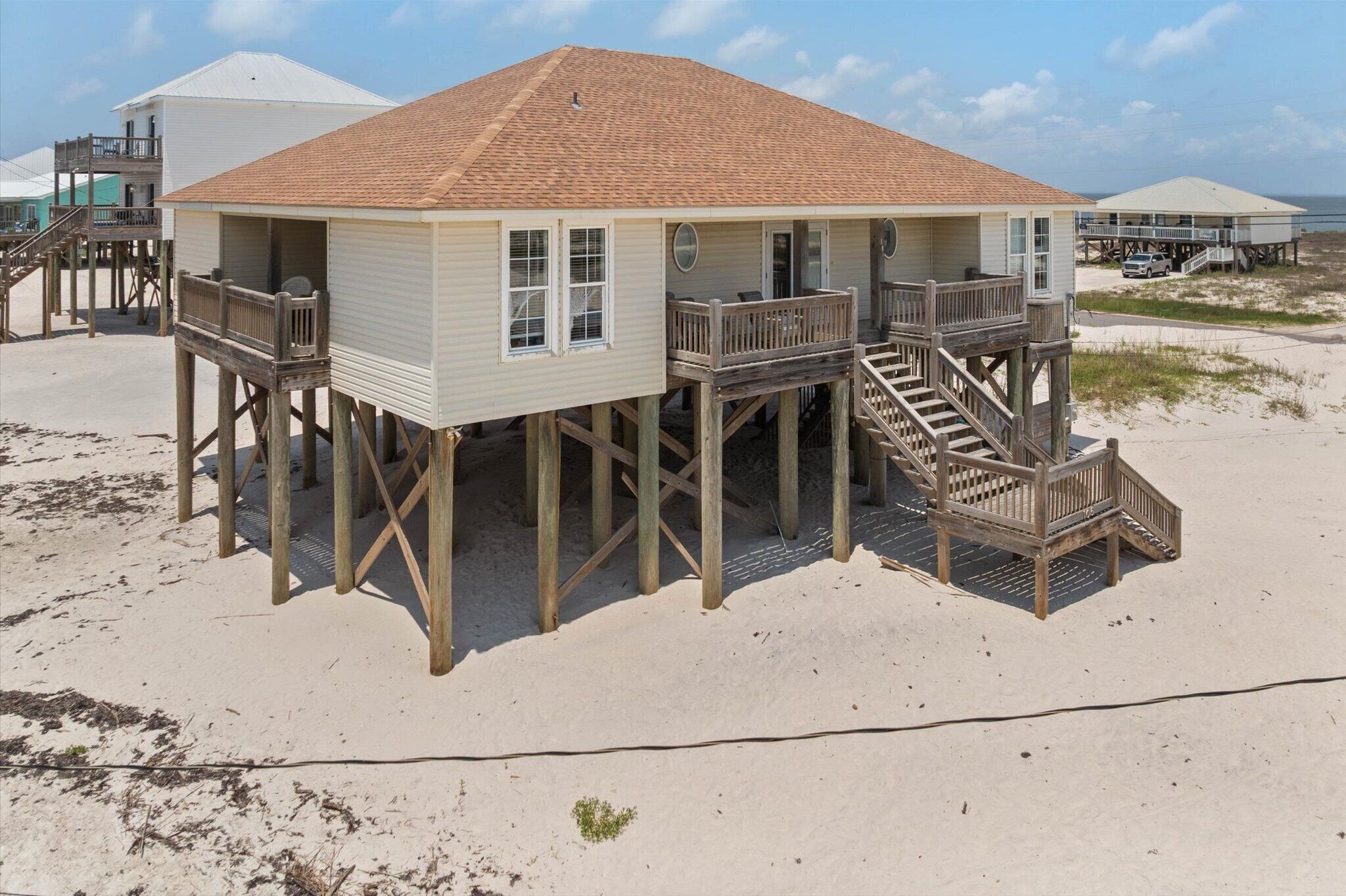 Une maison de plage avec une terrasse en bois, un escalier et une vue sur la plage.