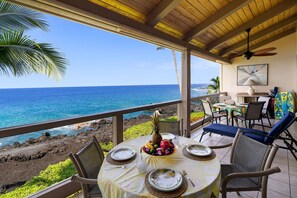 A covered outdoor dining area with a table set for two, overlooking a rocky coastline and the ocean. - Kksr#1304 Direct Oceanfront Top Floor unit with Loft 3 bedr/3 bath! (Kailua Kona)