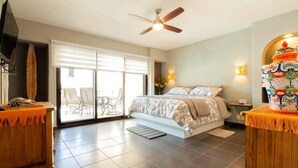 Une chambre à coucher comprenant un lit, un ventilateur de plafond, un téléviseur, une porte-fenêtre coulissante et un vase décoratif.