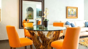 Un coin repas avec une table en verre et des chaises orange, un grand miroir et un tableau accroché au mur.