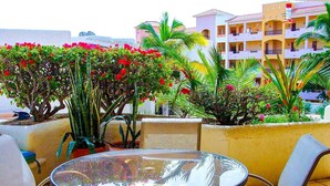 A round glass table with metal chairs in an outdoor setting with potted plants and a building in the background.