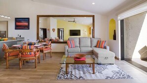 Un vaste espace de vie comprenant un canapé, une table à manger et des chaises. Un grand miroir reflète la pièce, et un téléviseur est fixé au mur.