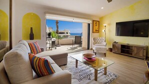 Un salon moderne avec un canapé, une table basse en verre, un téléviseur et un balcon offrant une vue sur la mer.