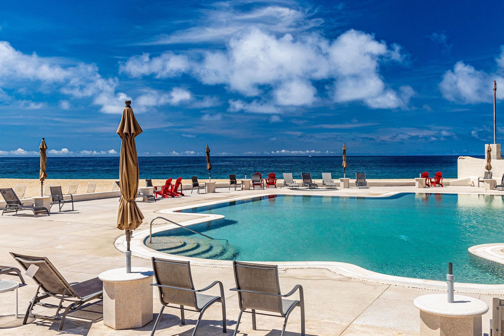 Un espace aménagé au bord de la piscine, avec des chaises longues et des parasols, offrant une vue sur l’océan.